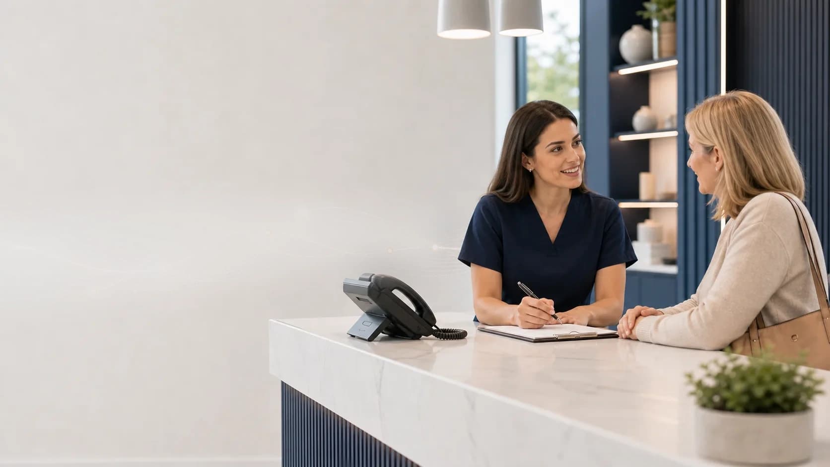 Reception team member helping a patient at the front desk while Greeta covers incoming calls